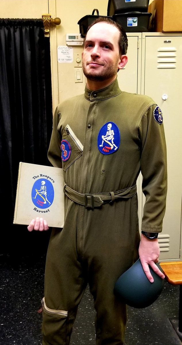 Jeremy, 2017, wearing one of Allen's actual flight suits — the 90th Squadron reaper emblem on the chest, matching the insignia throughout this book — holding Allen's own copy of “The Reaper's Harvest.”