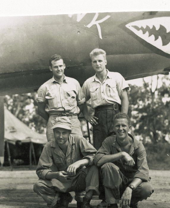 Two crewmen crouch in front of another shark-mouthed B-25 nose.