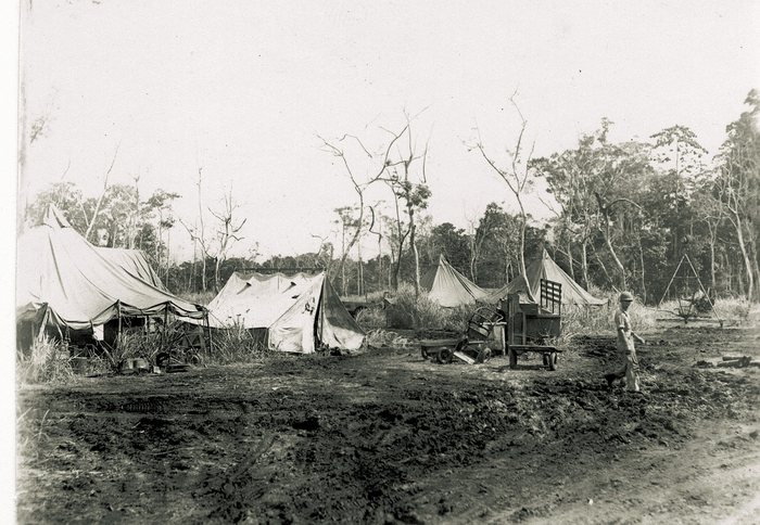 A muddy tent camp among the trees — everyday field conditions.