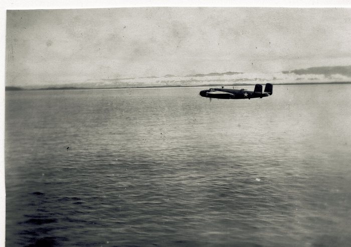 A B-25 Mitchell low over open water, photographed from another aircraft. The fin carries <b>11290[2]</b> -- the tail number for serial 41-1290[2], a B-25C from the same production block as Spook II, 41-12969. The national insignia is a plain white star in a disc with no side bars, which dates the frame before the end of June 1943, when the bars were added.