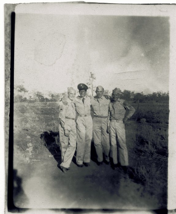 Four men arm in arm on a dirt track in open scrub country, Allen third from the left: three in shirtsleeves and soft caps, the second from left in a peaked service cap and necktie. The man at the left wears a senior sergeant's chevrons on his sleeve.