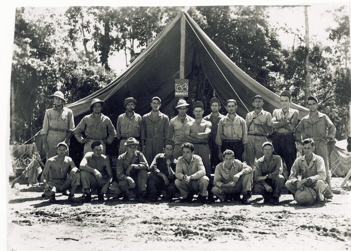 Nineteen men in front of an “Armament” tent sign with painted dice.