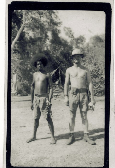 A local New Guinean man stands beside a serviceman in a pith helmet.