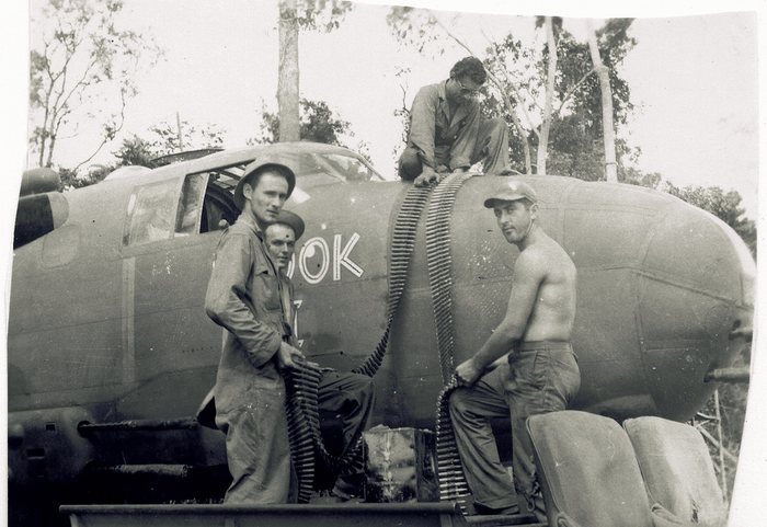Crewmen load a belt of ammunition into the top turret of a B-25. The letters 