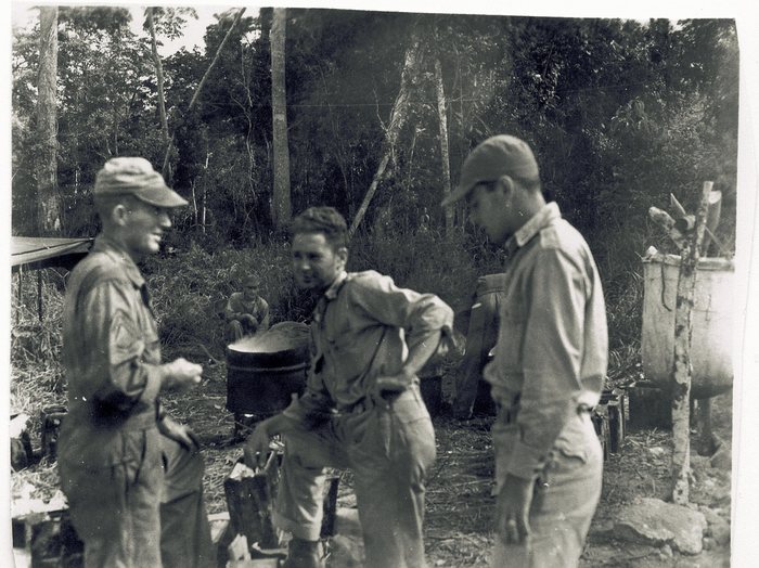 Servicemen gather around a large cooking pot at the outdoor kitchen.
