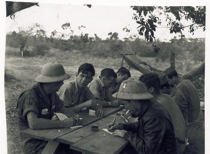 Servicemen sit at a wooden table writing letters home.