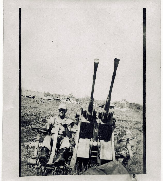 A twin-barrel anti-aircraft gun position, gunner at the ready — airfield defense at one of the squadron's bases.