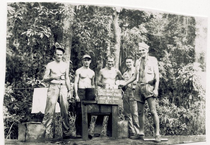 A hand-lettered camp canteen sign advertises beer and cigarettes.