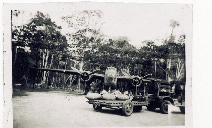 Bombs loaded onto a wheeled trailer beneath a B-25's open bomb bay.