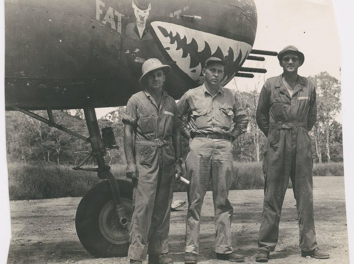 Three crewmen in front of “Fat Cat,” shark-mouth and bow tie visible.