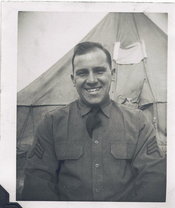 Allen, broadly smiling, in a wool service shirt and tie with three-chevron sergeant's stripes on both sleeves, in front of a pyramidal tent.
