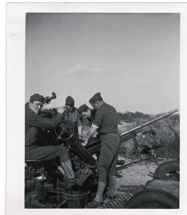 Four soldiers operate a mobile anti-aircraft gun mount in the field.