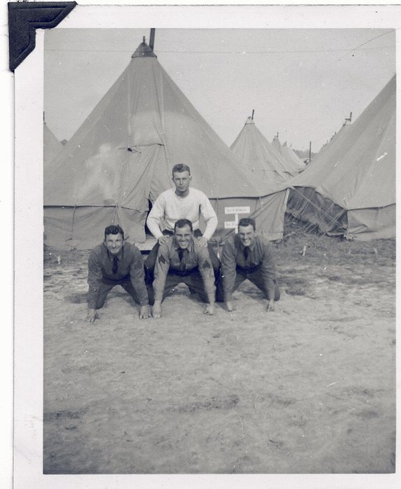 Soldiers clown around camp, one balancing on the backs of three others.