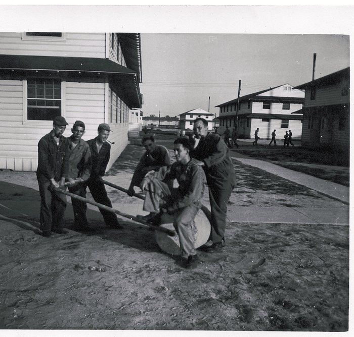Soldiers joke around a hand cart on a barracks street.