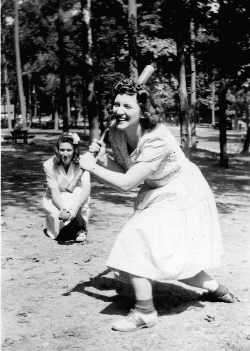 Catherine swings a bat playing ball with friends in a wooded park.