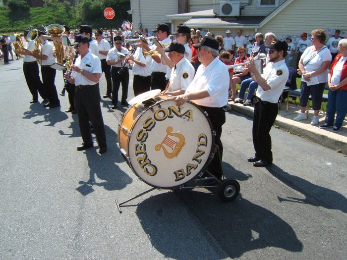 The same band from closer in, the "CRESSONA BAND" bass drum riding on its wheeled carriage as the drummer plays. A "STOP" sign marks the corner and the sign on the building behind is only partly readable, as "...RILL".