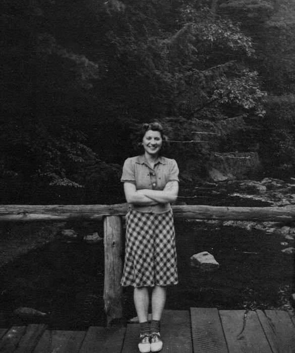 Catherine leans on a footbridge railing — Allen and Catherine dating, before the war.