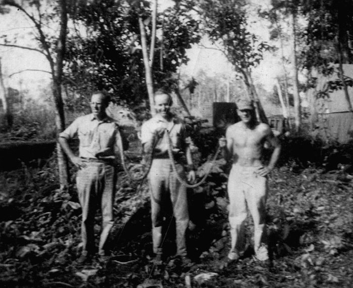 Three servicemen hold up a large snake they caught.