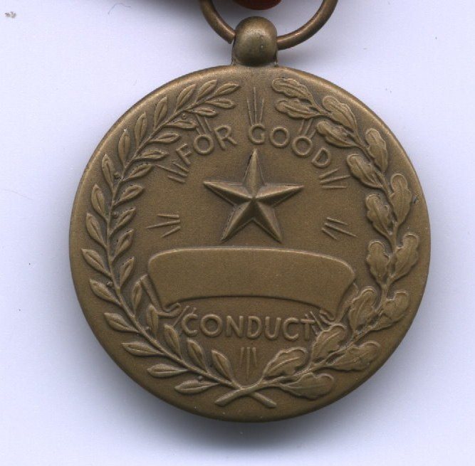 The reverse of a bronze medal, a wreath of laurel and oak encircling a five-pointed star above a scroll, with "FOR GOOD" lettered above the star and "CONDUCT" below the scroll. The scroll, which was meant to carry the recipient's name, is blank.