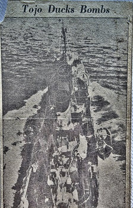 A newspaper clipping he kept, headed "Tojo Ducks Bombs". Beneath it is a coarse-screen press photograph, taken from the air almost directly overhead: what appears to be a ship under way on open water, its wake spreading astern, with dark patches in the sea to either side. The newsprint dots are heavy and no marking or name can be read. Credit: the newspaper is not named on the cutting; from his own collection.