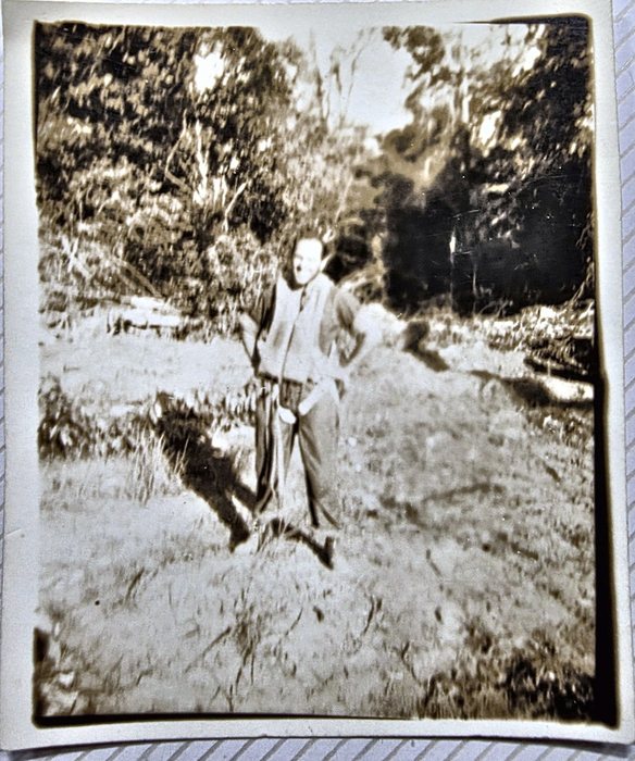A serviceman stands in rough grass with scrub and trees behind him, wearing a bulky sleeveless vest over his shirt and trousers, hands at his waist. The back reads "Me in life vest and parachute" above a fast signature read only tentatively as "Alex Garcia" -- since the writer calls the man in the picture "Me", the signer is very probably the man shown; a US Army censor stamp is on the back.