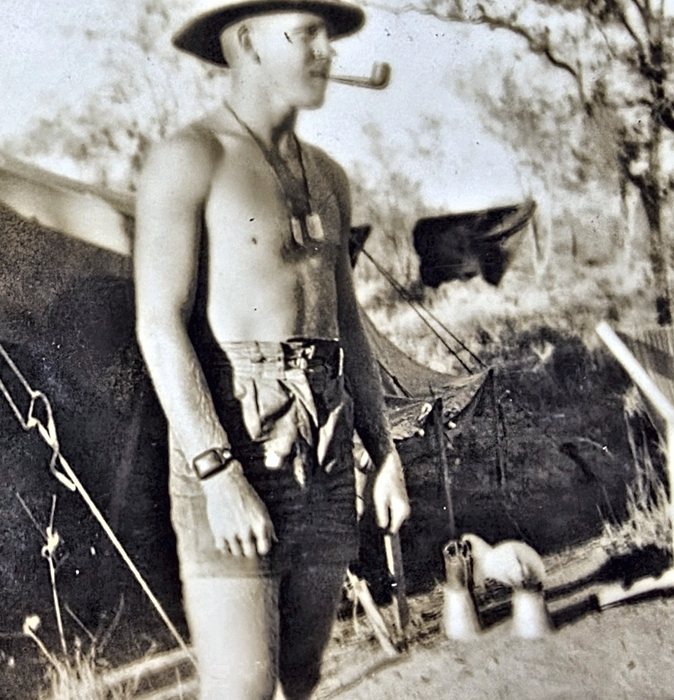 A bare-chested serviceman in a broad-brimmed campaign hat stands among pitched tents with a pipe clenched in his teeth, dog tags on a chain, a wristwatch on his right wrist and a slender tool handle gripped in his left hand. Named on the back as William Gatzman, with the home town written "Bugaloosa Ala." -- as given, though Bogalusa is in Louisiana.