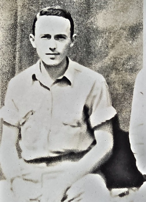 A young man sits for the camera in a light short-sleeved open-collar shirt, hands folded in his lap, with the sleeve and shoulder of the man beside him cropped away at the right edge of the print. Named on the back as Henry "Hank" Mille-- of Pittsfield, Massachusetts, the surname running off the edge of the print; Miller is the likely completion but cannot be read.