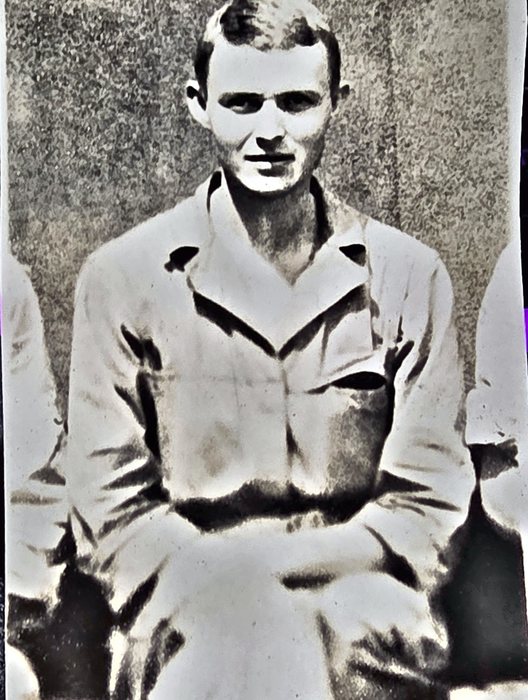 A young man sits square to the camera in a light open-collar work shirt with a flapped breast pocket, arms low in his lap and the arms of the men on either side cropped at the edges of the print. Named on the back as James Frenell[?] of Cairo, Illinois -- the surname is drawn F-r-e-n-e-l-l and Fennell may be the intended spelling.