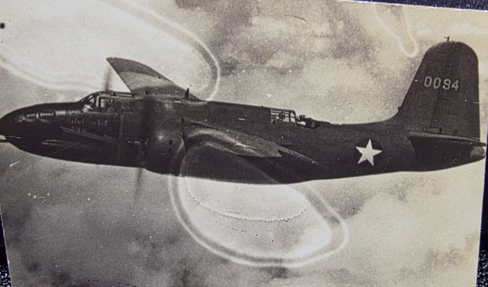 A twin-engined bomber photographed in flight from another aircraft, banking away so that the far wing rises above the fuselage line. The fin carries the number 0094, and a line of script nose art runs below the cockpit which the print is too coarse to read with confidence. The national insignia on the rear fuselage is a plain white star on a dark disc with no side bars, which places the frame before late June 1943.