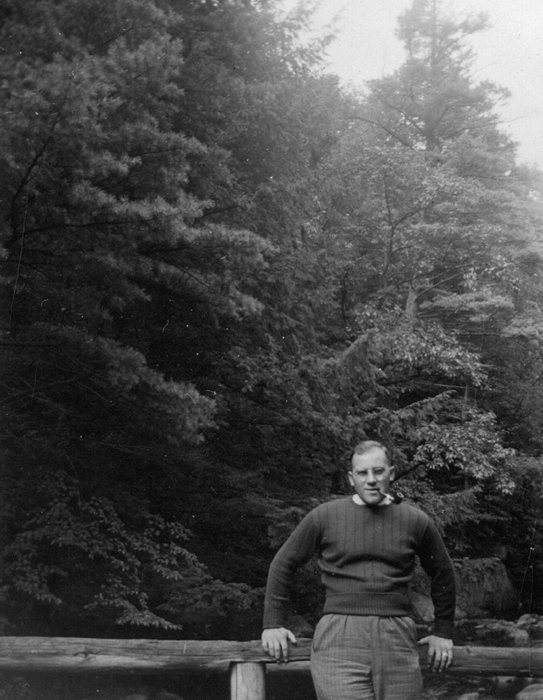 Allen leans on a wooden bridge railing, smoking a pipe — the same courtship-era outing.
