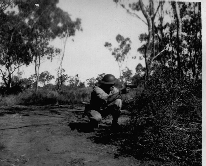 Allen crouched, aiming a pistol in the Australian bush.